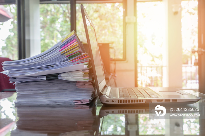 laptop and document stack on office desk with sun flare