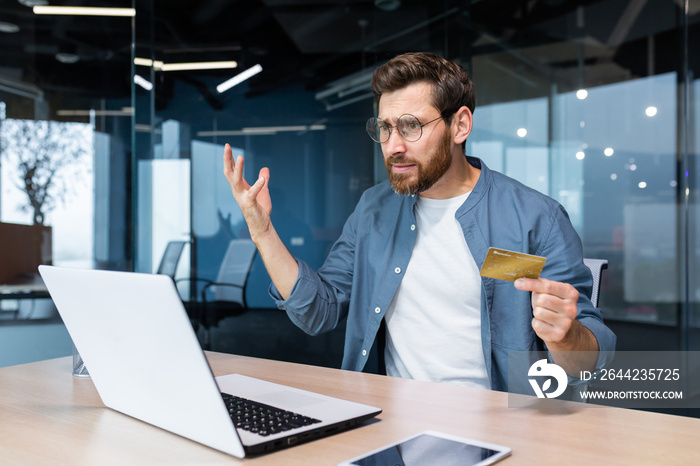 Bankruptcy, financial problems. Angry and worried young man sitting in the office, holding a credit 