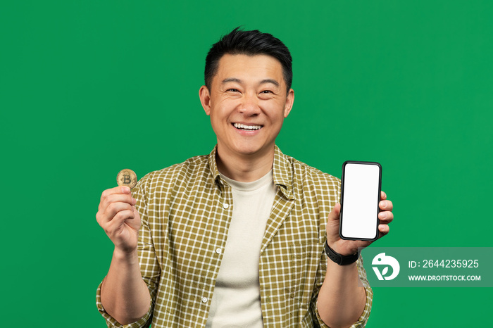 Mature asian man holding golden bitcoin coin and showing cellphone with white screen, recommending o