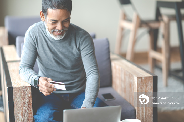 Attractive bearded hipster asian father or Hispanic old man using Laptop and credit card payment sho