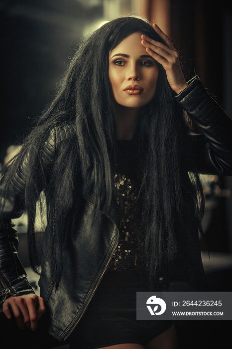 Dark haired model is posing in a dark studio with a mirror