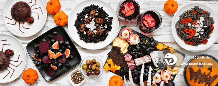 Halloween dinner party table scene over a white wood banner background. Top view. Spooky black risot