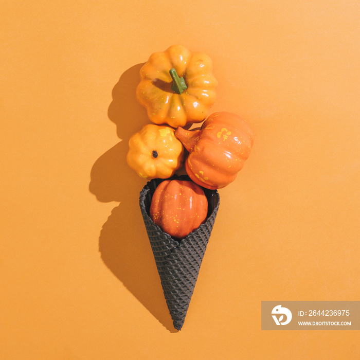 Icecream made with black ice-cream cone and pumpkins on orange background. Halloween sweet dessert. 