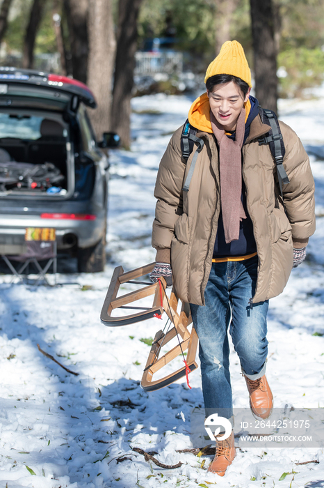 雪地上步行拿着雪橇的青年男人