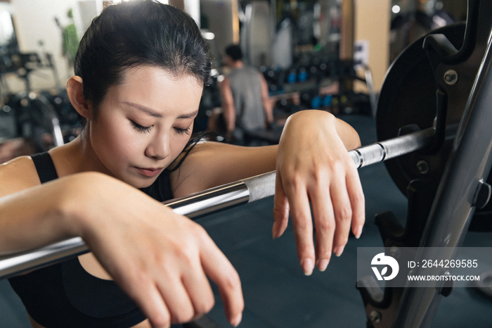 健身房里年轻女子趴在杠铃上休息