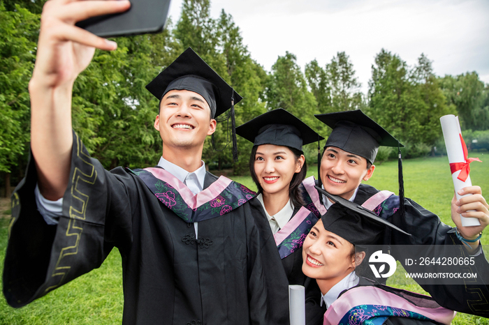 四个身穿学士服的大学生用手机自拍