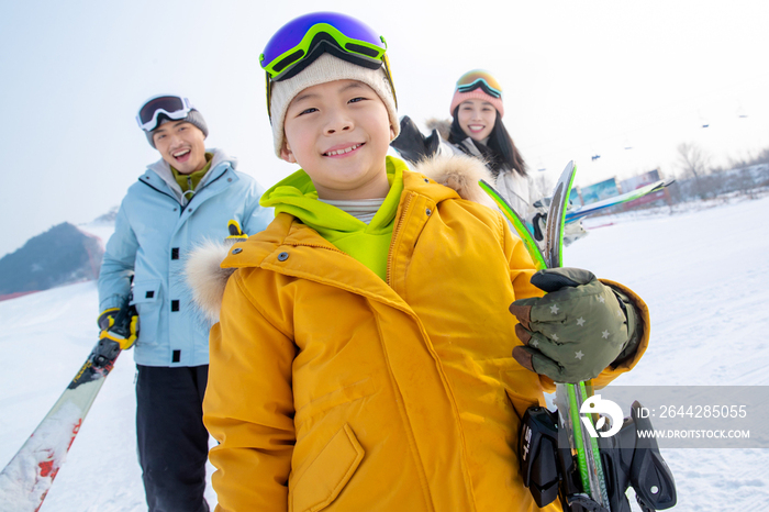 雪场上拿着滑雪板的一家三口