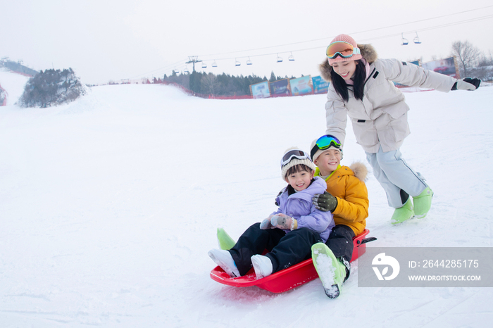 滑雪场上妈妈推着坐在雪上滑板的孩子们