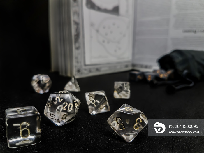 Set of transparent dice for role play, placed on a black surface, with a manual and a bag of dice in the background.