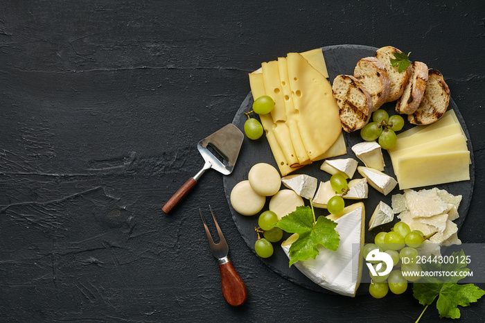 Top view of tasty cheese plate with fruit, grape on a circle kitchen plate on the black stone background, top view, copy space. Gourmet food and drink.
