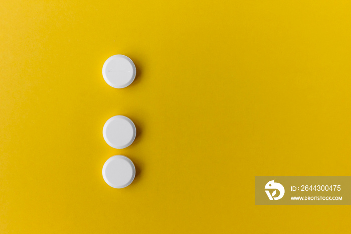 three white round pills on yellow background with copy space