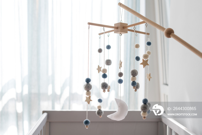 Baby crib mobile with stars, planets and moon. Kids handmade toys above the newborn crib. First baby eco-friendly toys made from felt and wood hanging in light room. Space for text