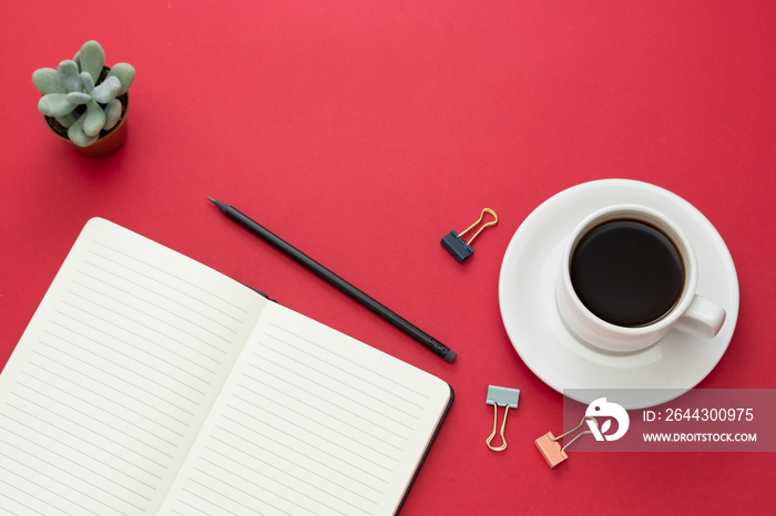 Table top, working desk with open notebook and coffee cup on red background. Copy space for text.