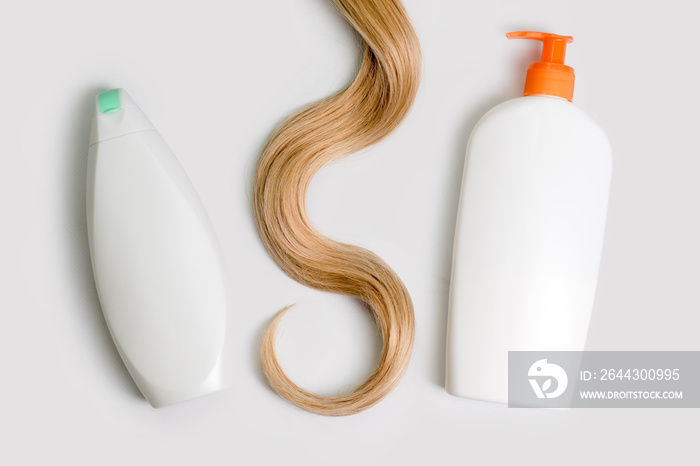 Shampoo and conditioner bottles and lock of curly blonde hair isolated on light background, top view. Flat lay, copy space for text. Hair care cosmetics, beauty haircare products, hair treatment.