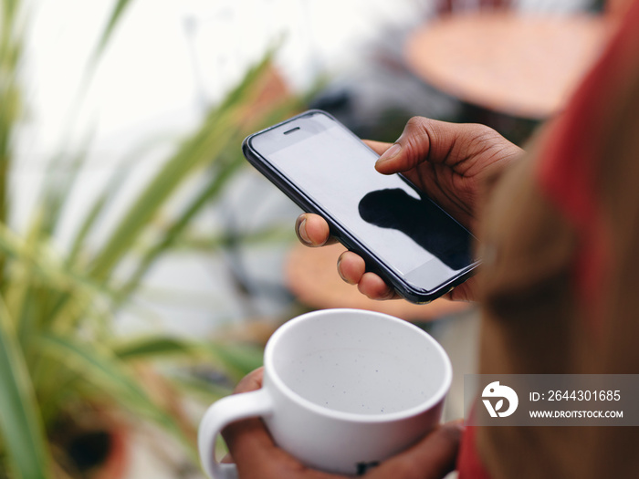 Close-up of mans hands holding smart phone and mug