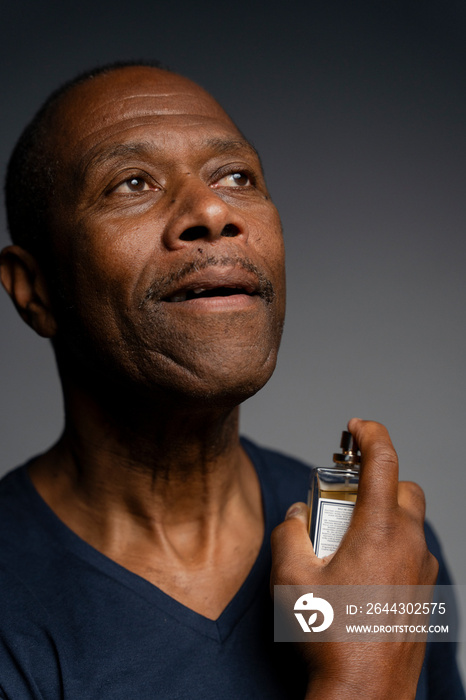 Portrait of man putting on perfume against gray background