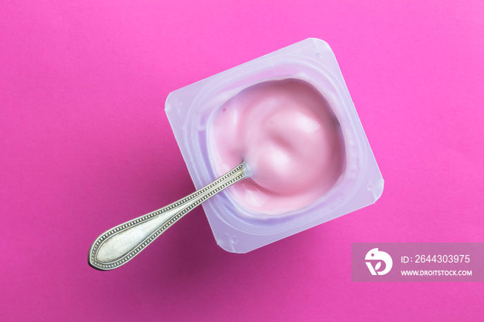 Yogurt cup with pink yoghurt and spoon on bright pink background