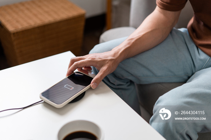 Technology Concept A person with his light blue jeans sitting on the couch and trying to charge his smartphone on the wireless battery charger