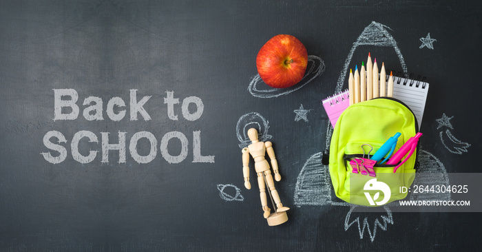 Back to school concept with small bag backpack, school supplies and rocket sketch over chalkboad background. Top view from above