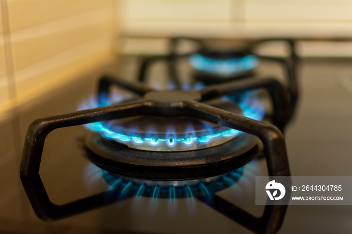 Natural gas burning on kitchen gas stove in the dark. Panel from steel with a gas ring burner on a black background, close-up shooting