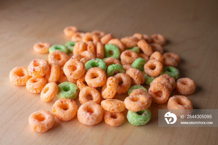 pile of no brand cheerios style round circles breakfast cereal in orange and green on a wood table in natural light