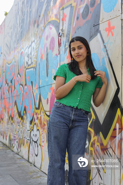 Portrait of young woman standing in front of graffiti wall