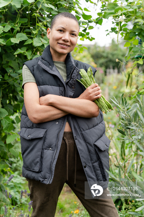 Portrait of woman with bunch of homegrown green bean in urban garden