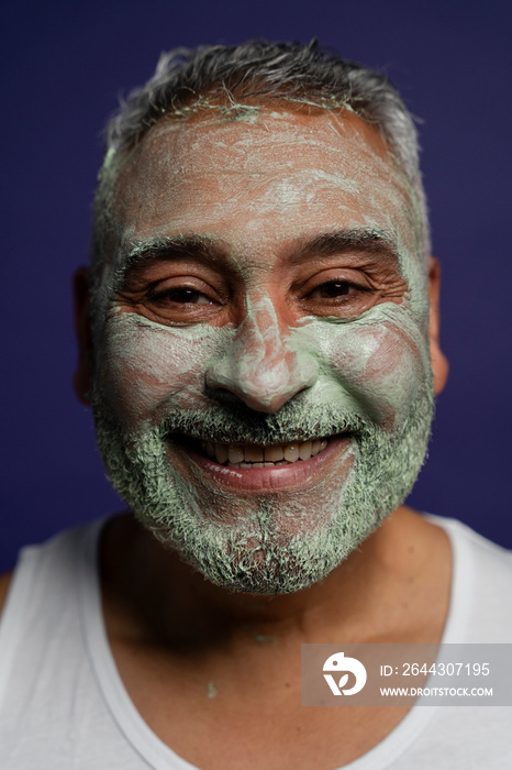 Portrait of smiling man with facial mask against purple background