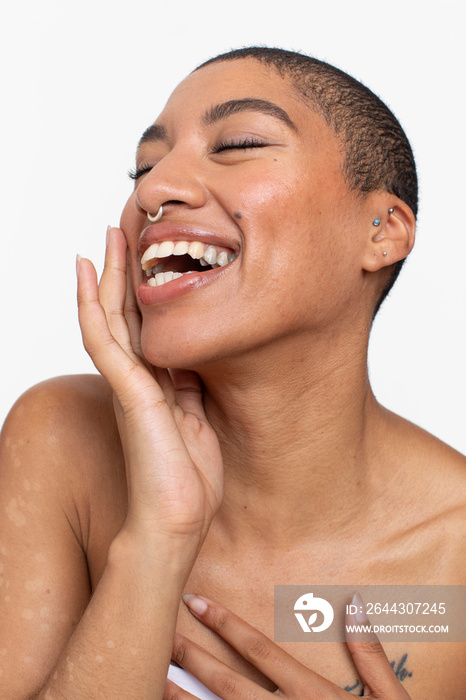 Studio portrait of woman with short hair and nose ring laughing with eyes closed