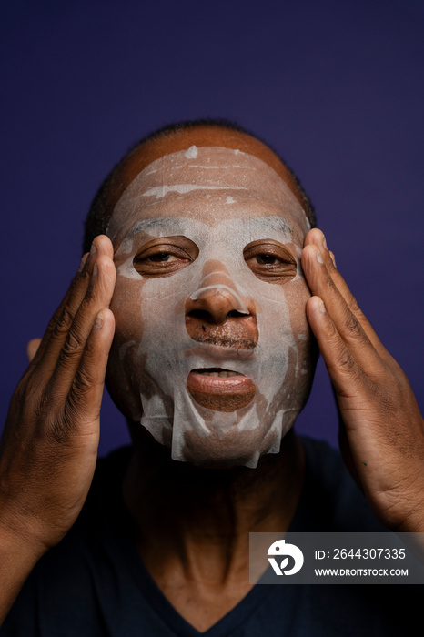 Portrait of man applying facial mask against purple background