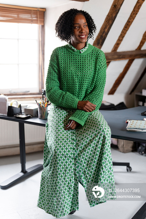 Portrait of smiling businesswoman looking away while sitting on desk in office