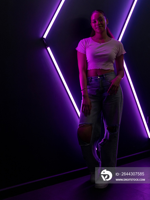 Portrait of young woman against wall with neon lights