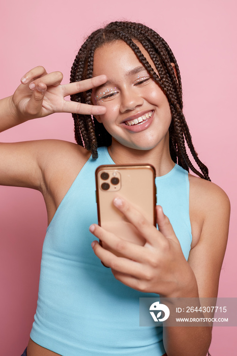 Studio shot of smiling girl with braids taking selfie