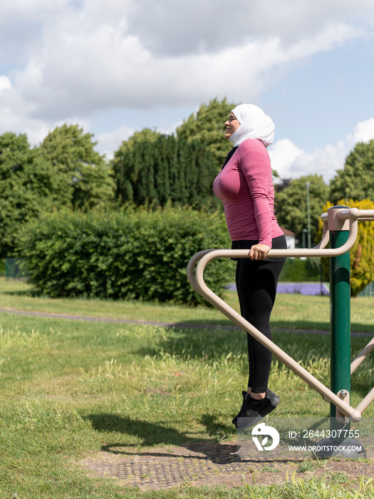 UK,Sutton,Smiling woman in headscarf exercising at park gym