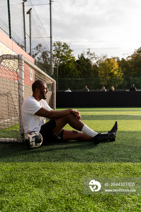 Man with ball sitting next to soccer goal