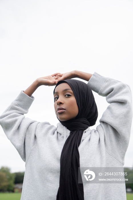 Portrait of woman in hijab standing outdoors with arms raised