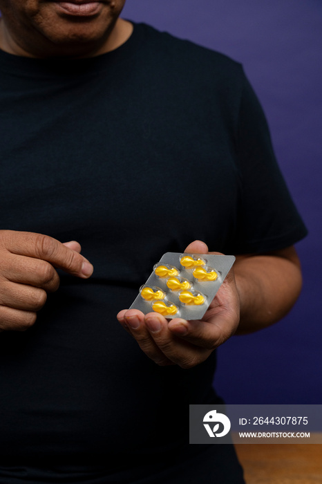 Man holding blister with yellow capsules against purple background