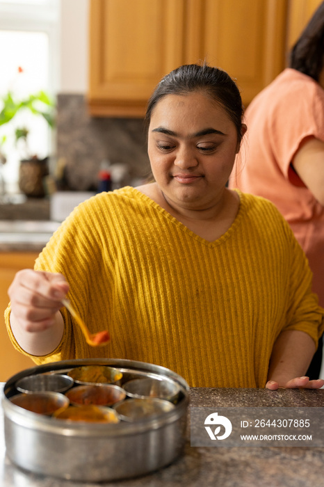 Woman with down syndrome adding spices while cooking in kitchen