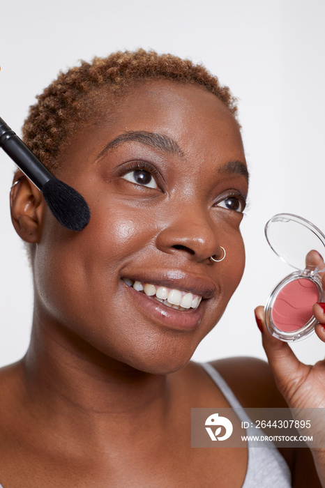 Studio portrait of smiling woman applying blush