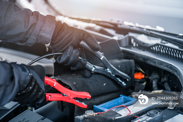 Hands charging car battery with electricity trough electric cables. Vehicle jumper cable cars starting or connection in winter time.