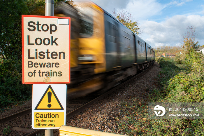 Train level crossing safety sign. Stop Look Listen warning sign crossing train tracks. selective focus on warning sign with a train passing with motion blur. Rail safety beware of trains signage.