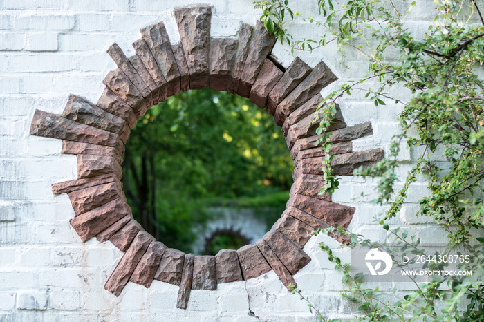 A round hole in a brick wall in a park looks like a portal