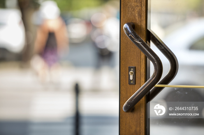 Close-up of plastic or wooden modern brown door with transparent glass surface and big metal handle on blurred bright copy space bokeh background. Entrance, exit, office or hallway.