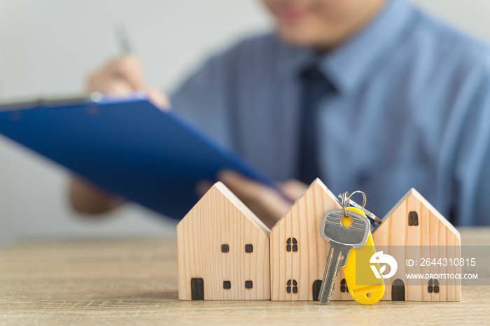 House Wooden model and Key in real estate , seller or buyer , loan concept with blur loan employee or realtor he’s checking details about the sale of the house ,home Mortgage or home lone.