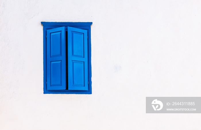 White wall with blue window and closed shutters. Greek style.