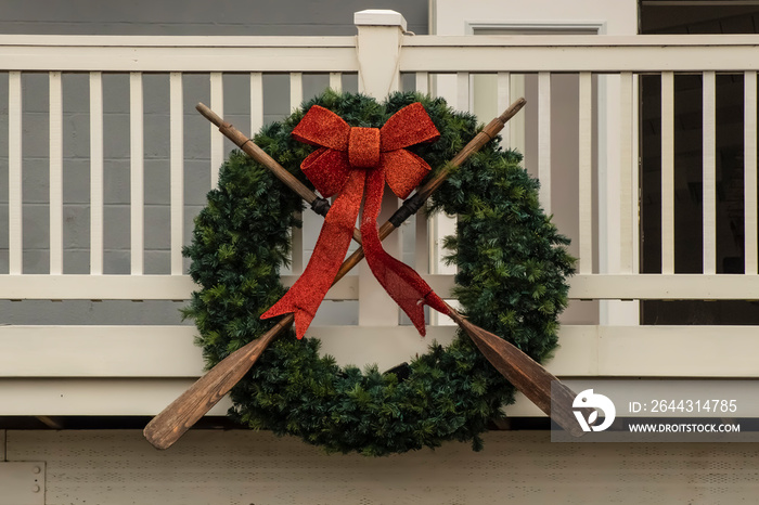 Nautical wreath with old worn oars and sparkly red bow mounted on wooden porch - closeup