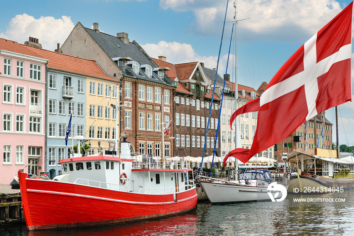 Nyhavn a 17th century harbour in Copenhagen with typical colorful houses and boats with national flag of Denmark on the first ground.