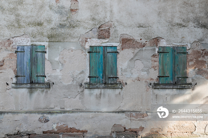 Cracked old cement wall with rough surface and three old windows in the old house