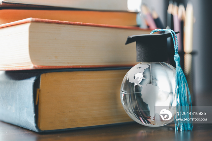 Graduate study abroad program concept : Black graduation cap on a globe map and books, depicts knowledge can be learned online anywhere and everywhere, even in universities or campus around the world.