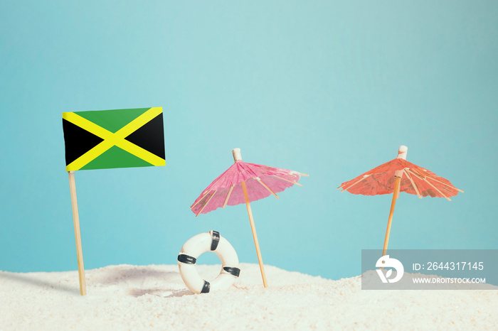 Miniature flag of Jamaica on beach with colorful umbrellas and life preserver. Travel concept, summer theme.